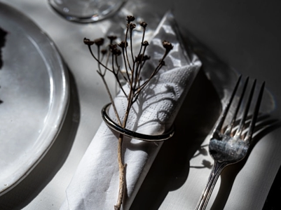 På ett bord ligger en silvrig servettring med en servett och en blomma instoppad i sig. Till vänster ligger en tallrik och till höger ligger en gaffel.
