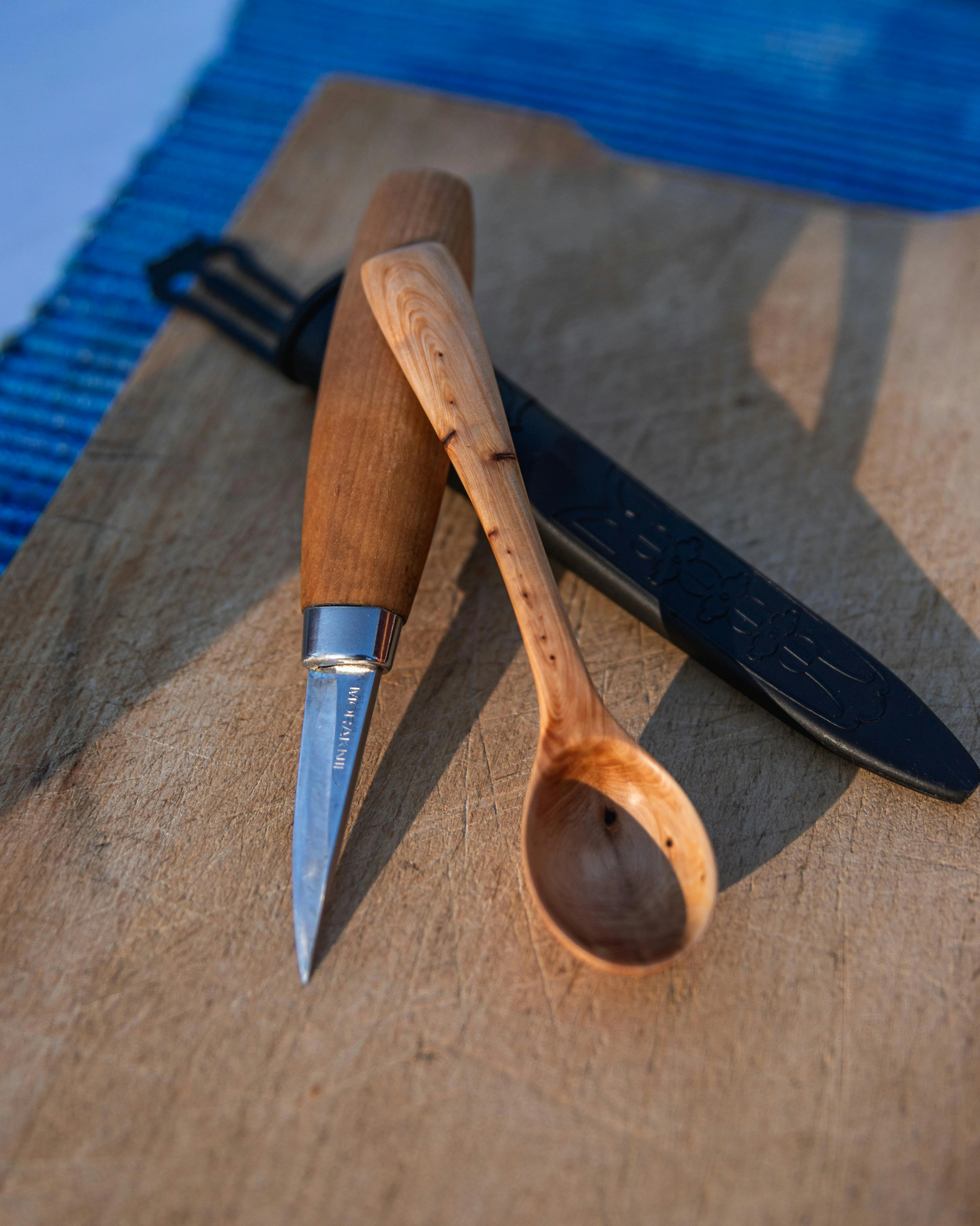 Liten kniv med trähandtag som ligger på ett bord bredvid en täljd sked