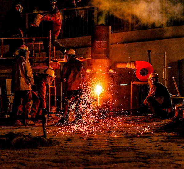 fyra personer klädda i jackor, byxor och skyddshjälmar vid byggställningar och eld som sprutar i mitten av bilden