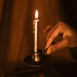 hand håller i en svart låg ljusstake med ett silverfärgat tänt ljus