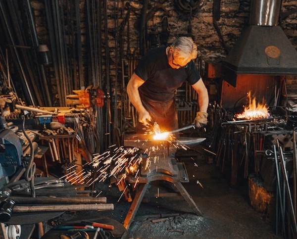 man står i en smedja och smider en metallstång