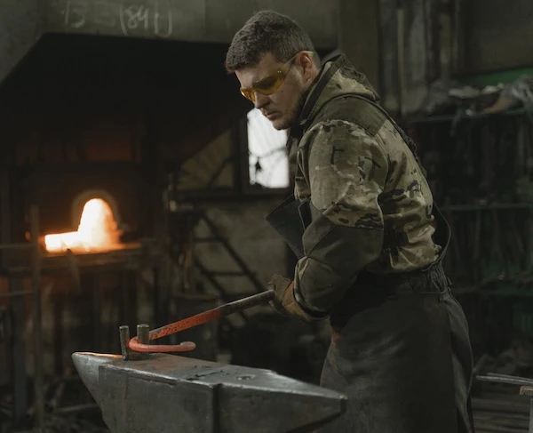 man smider en glödande metallstång runt två metallpinnar som sticker upp från ett större metallobjekt