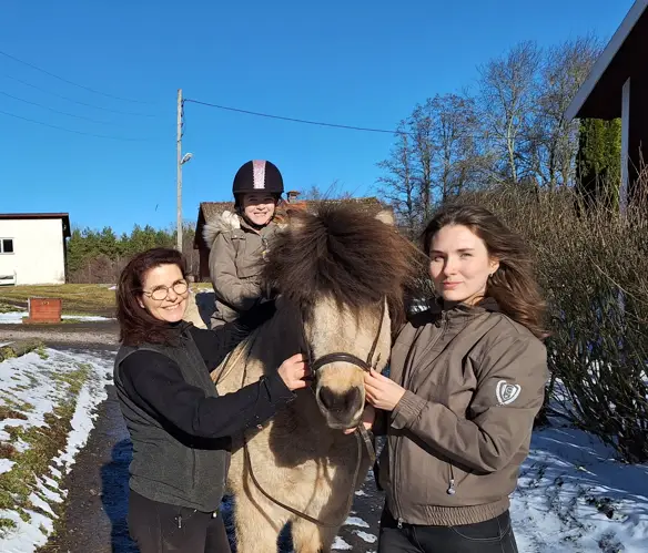 En häst med en liten flicka på ryggen och har en kvinna på varsin sida