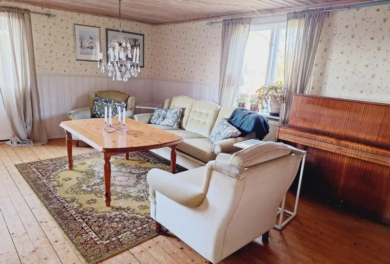 Ett vardagsrum med en soffa, två fåtöljer och en piano